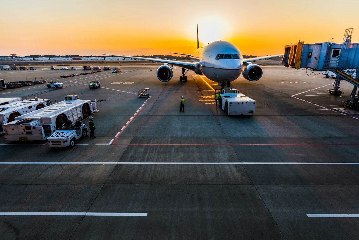 A wide-body aircraft parked at an airport gate under a low winter sunrise