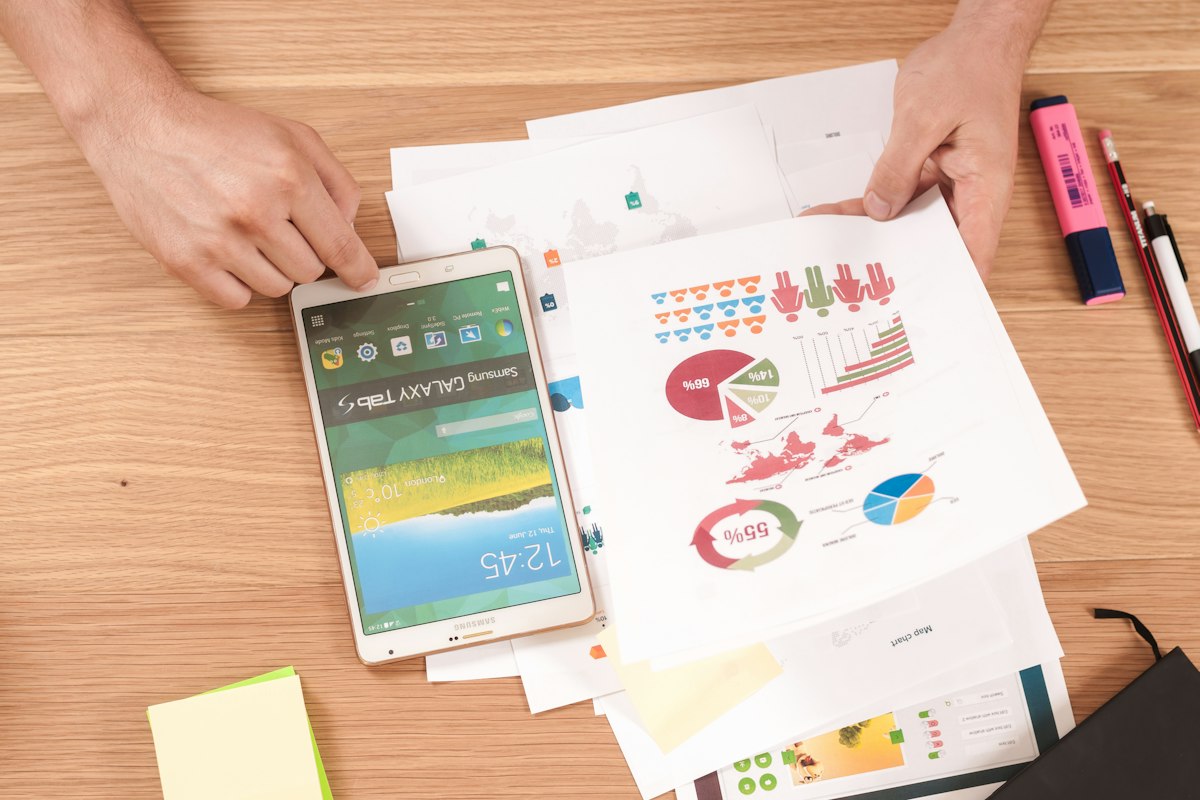 Hands resting on a desk beside printed pie charts, a smartphone and colourful sticky notes used for budget planning