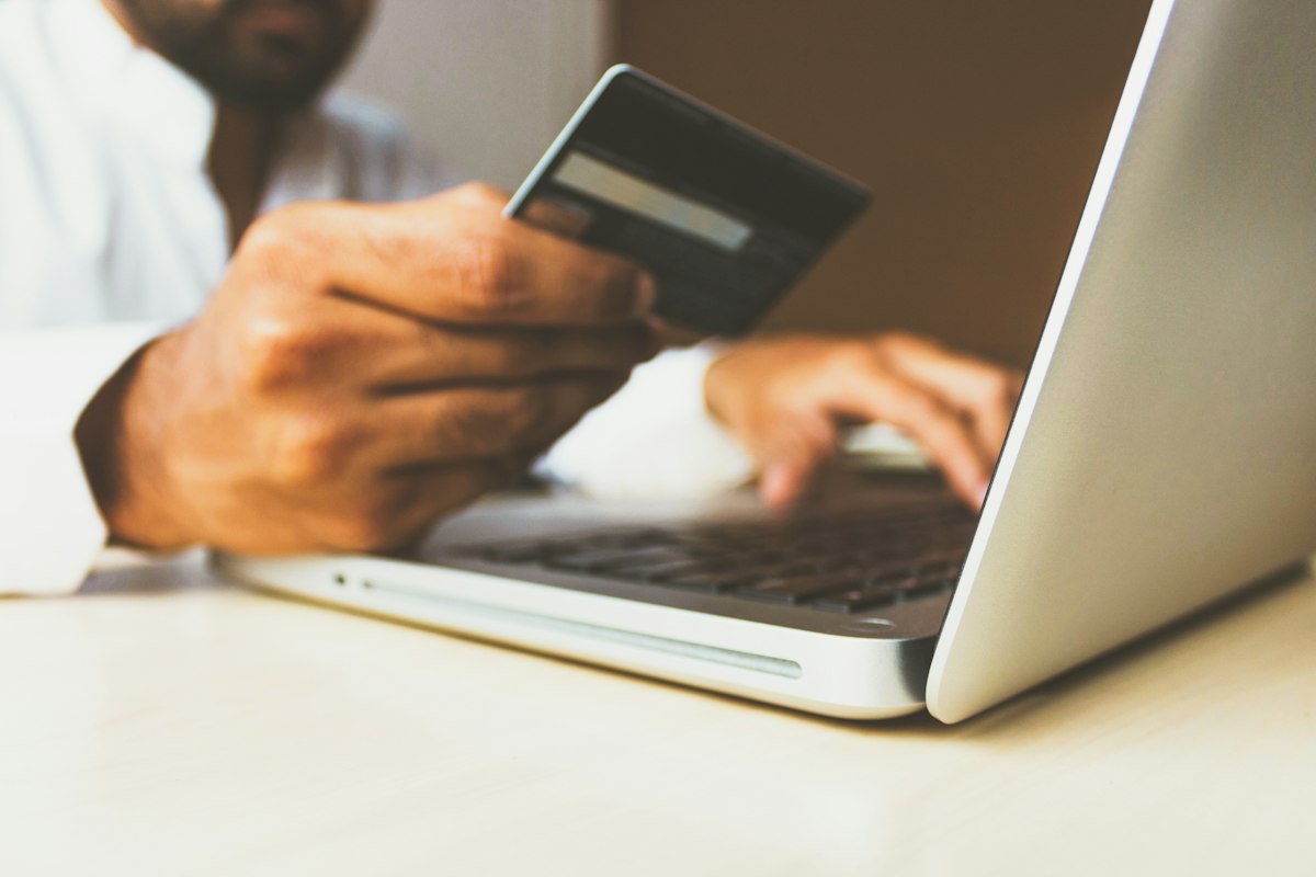 Person holding a credit card in one hand while typing on a laptop keyboard with the other