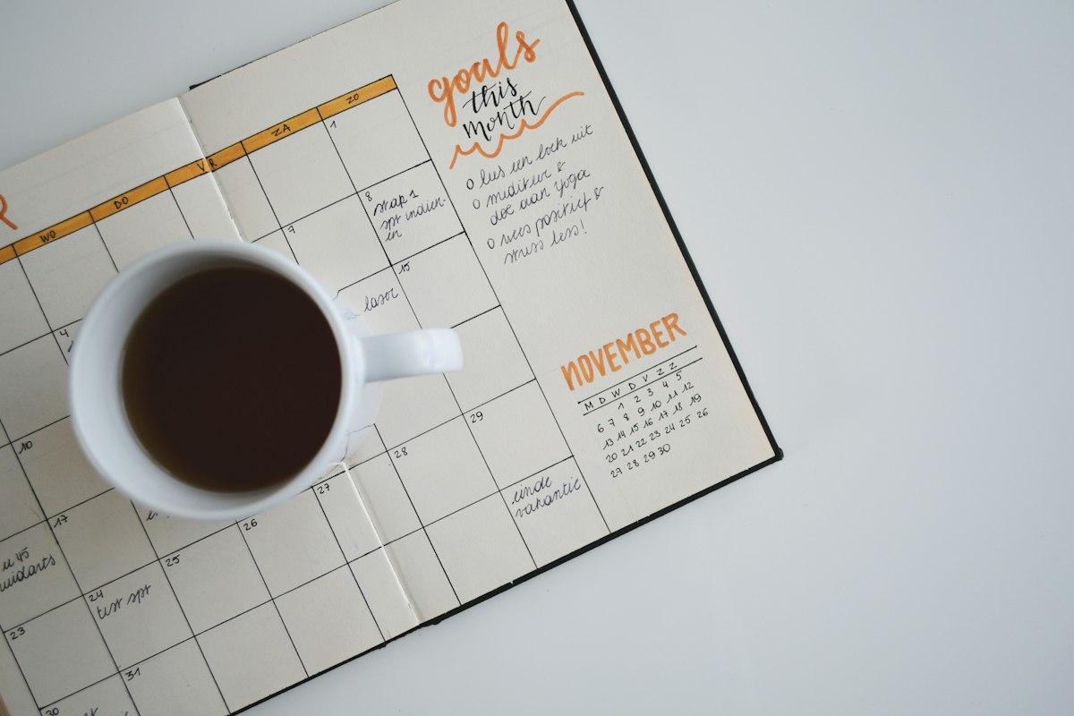 Open monthly planner page with the word goals handwritten at the top, next to a cup of black coffee