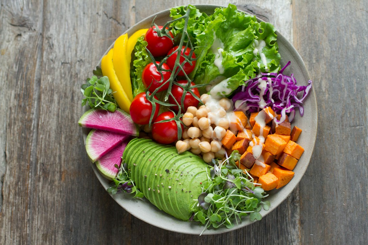 A colourful bowl of salad leaves, chickpeas, sliced avocado, cherry tomatoes and roasted sweet potato