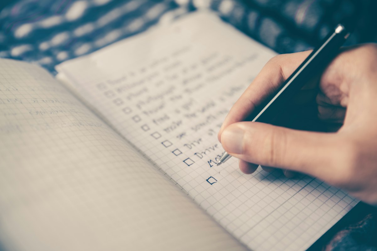 A hand ticking items off a handwritten checklist in an open notebook