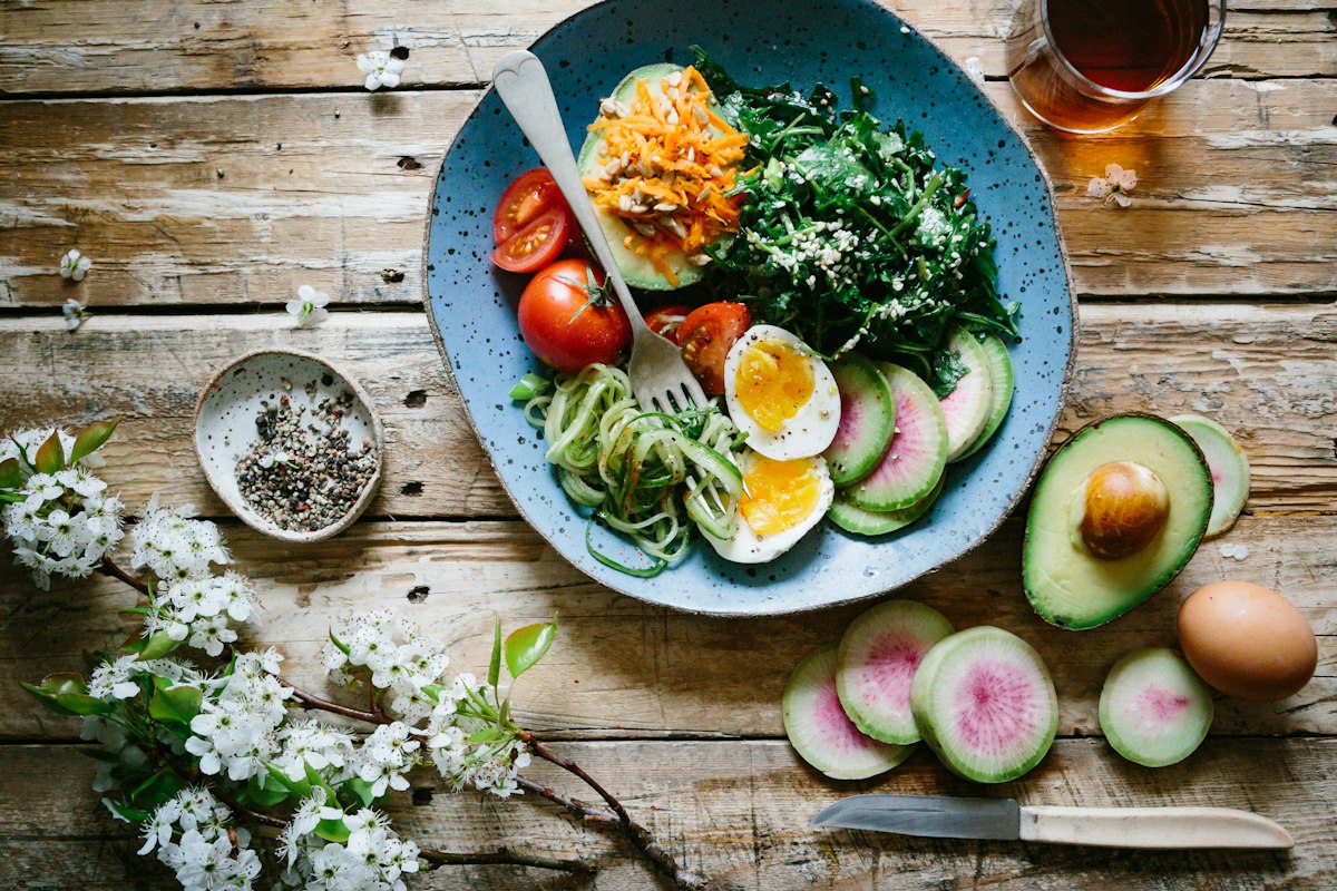 Wooden table with a bowl of salad, sliced avocado and boiled eggs